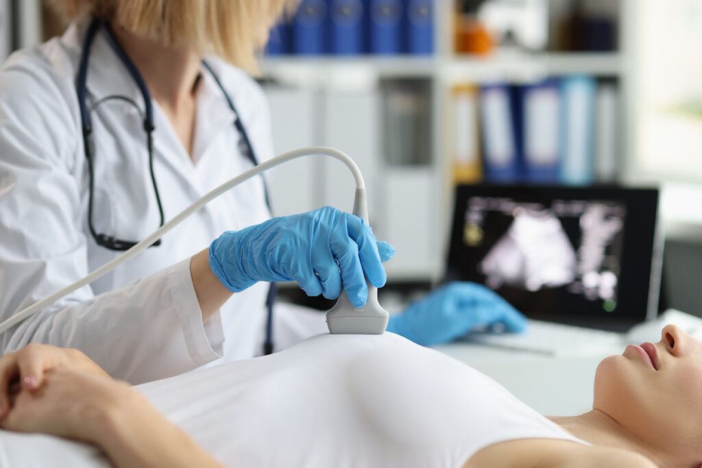 Doctor makes breast ultrasound to young woman in clinic closeup. Diagnosis of breast diseases concept