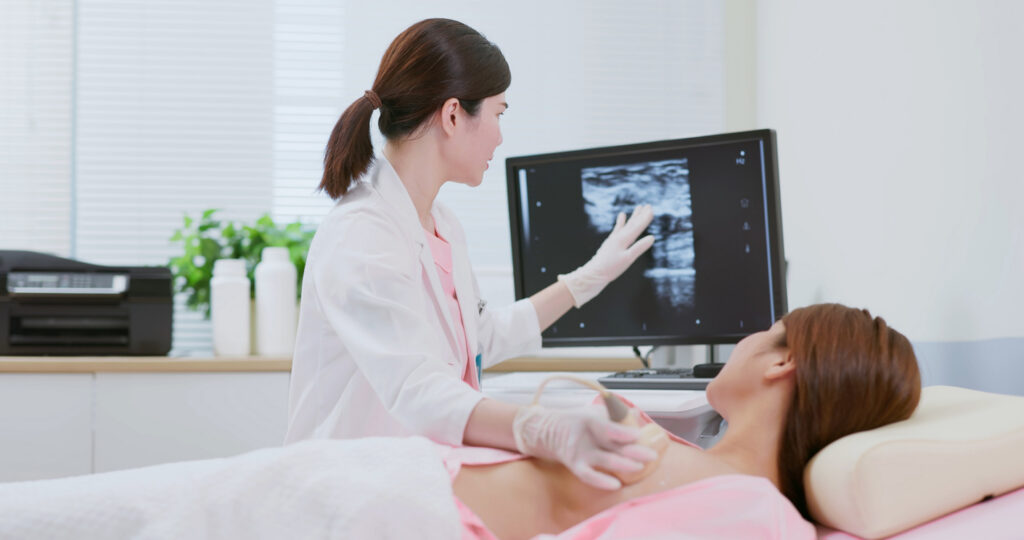 Close up of doctor using ultrasound scanner performing examination of breast for her patient - cancer awareness feminine health medical concept