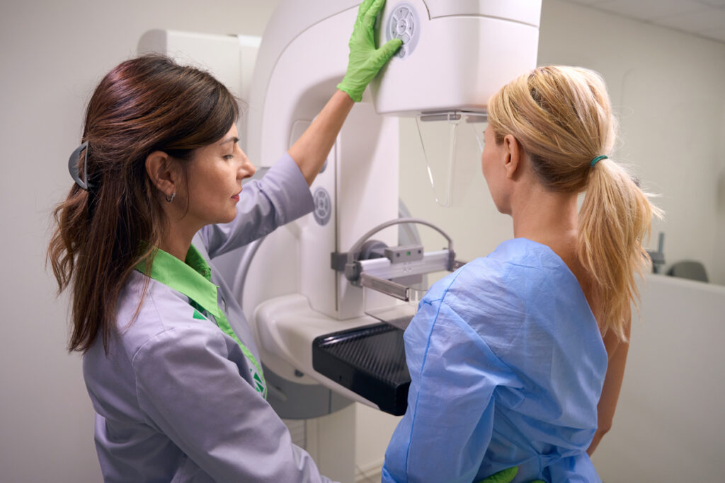 Radiographer using control panel for positioning compression paddle of mammography machine against client chest wall